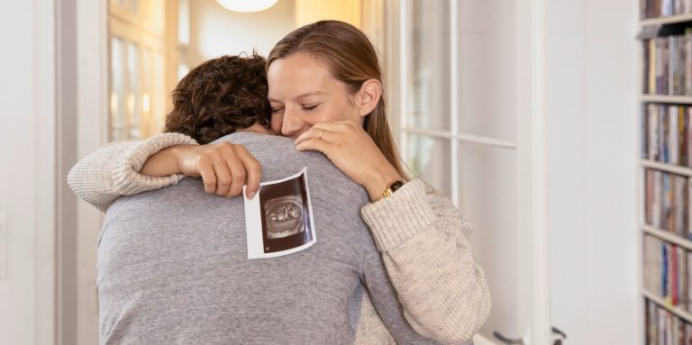 Frau mit Ultraschall-Bild in der Hand umarmt Mann